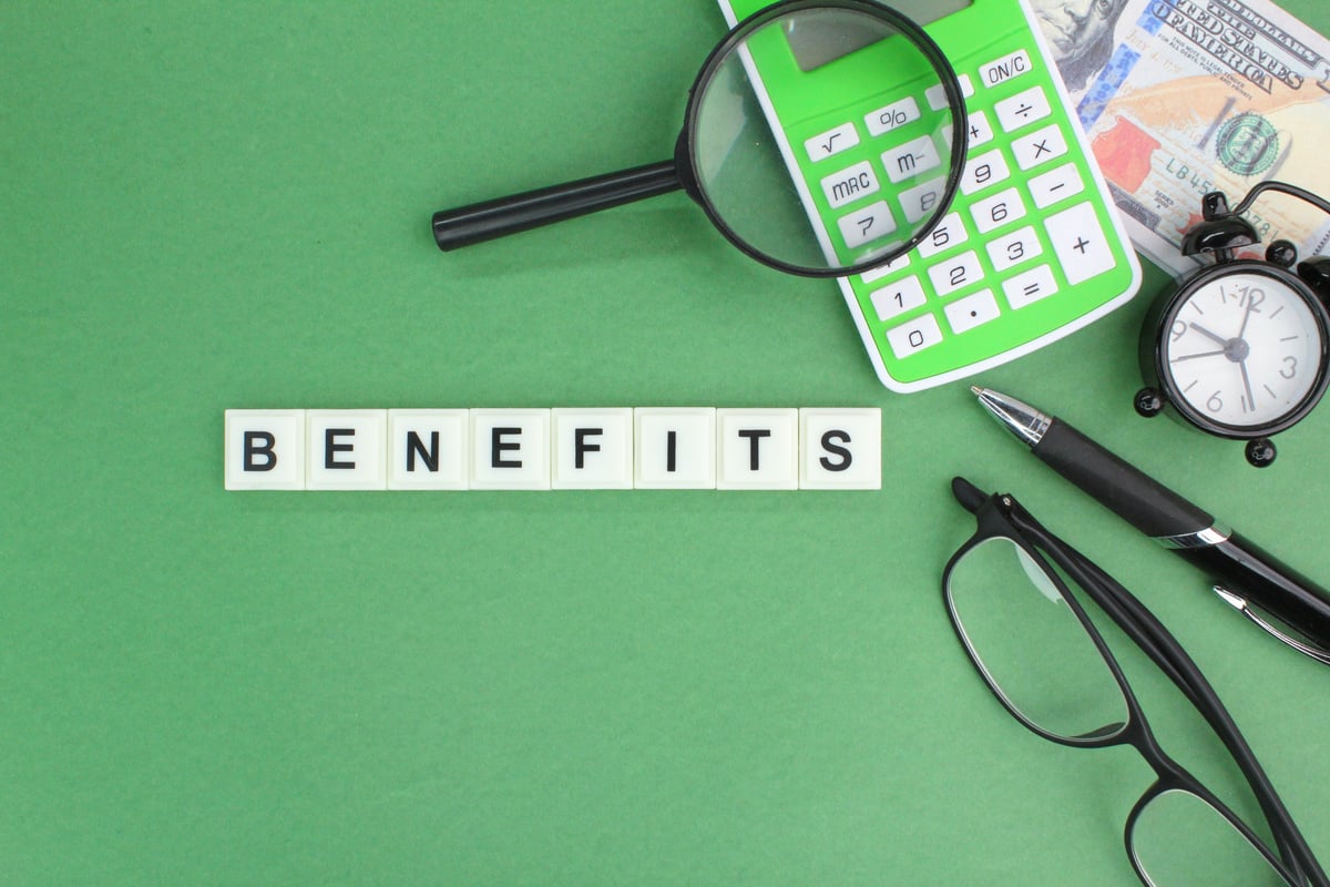 Wooden blocks spelling “benefits” next to calculator and money