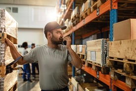 male-warehouse-worker-communicating-with-someone-walkietalkie-while-standing-shelfs-distribution-warehouse